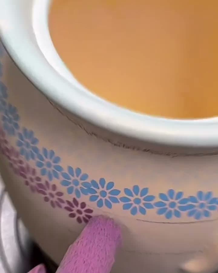 A sponge printing rows of tiny flowers onto a bisque pot on a banding wheel